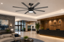 A large and modern black ceiling fan with a central light fixture installed on the ceiling of a luxury hotel lobby. The lobby features a wood reception desk with the 'HARBORVIEW HOTEL' logo, a stone accent wall, and a beige sofa in the foreground.